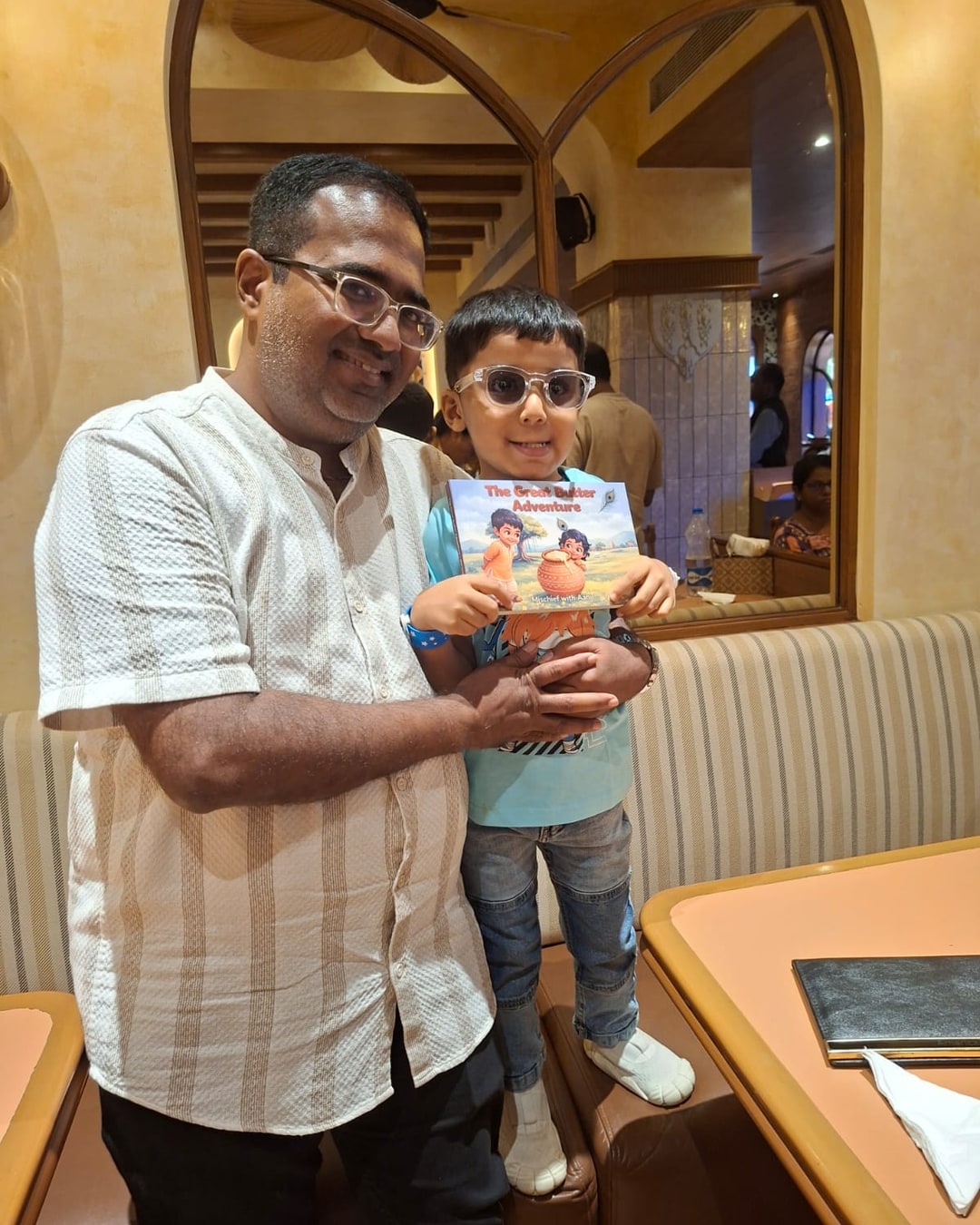 Aahir grinning with his uncle Mehul, holding the hardcover of The Great Butter Adventure gifted to him, his own name on the cover